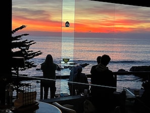 A view of the ocean at sunset with silhouettes of people on a balcony.