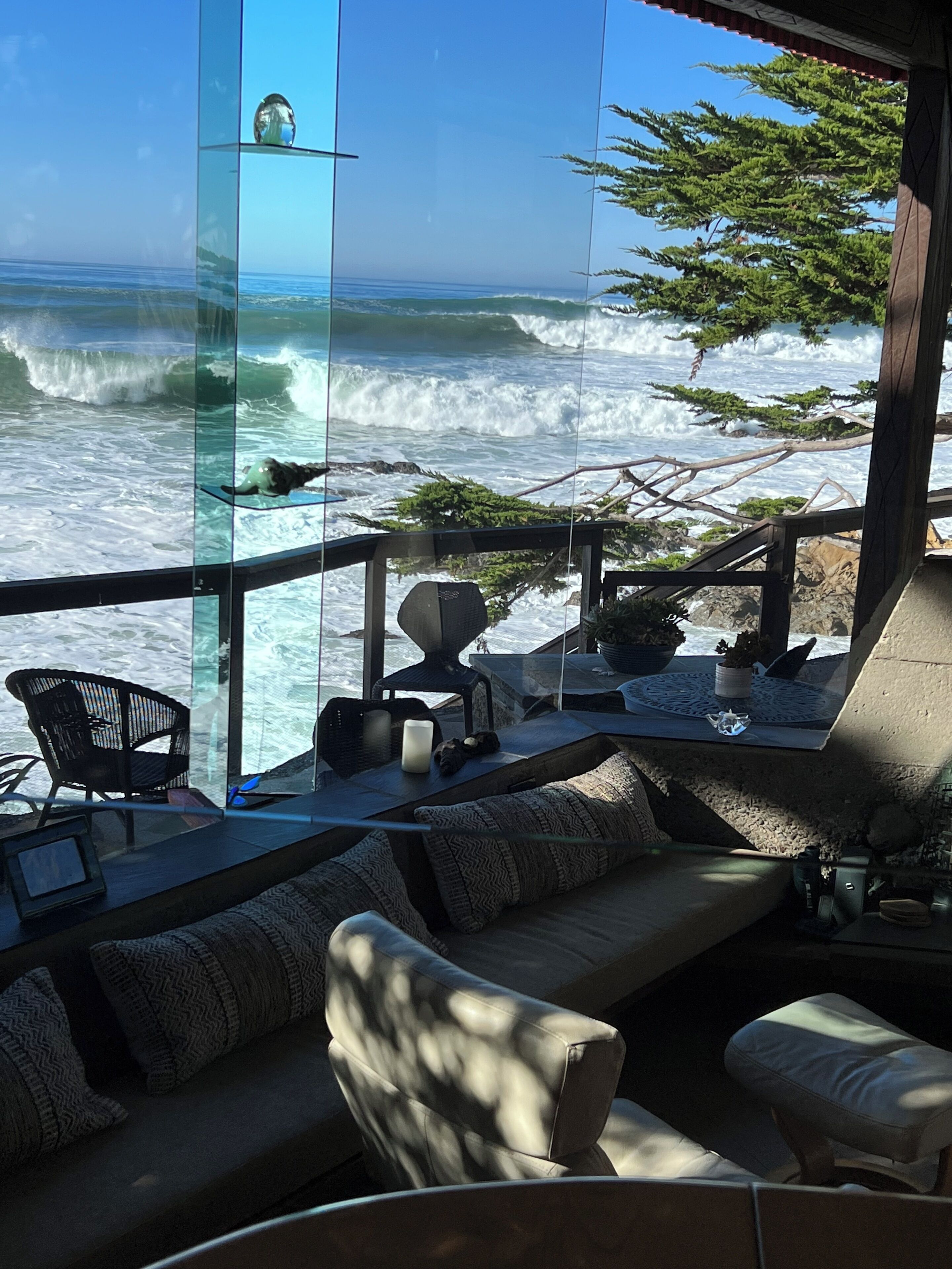 Vista al mar desde un balcón con paredes de cristal, que incluye un sofá, sillas y una mesa.