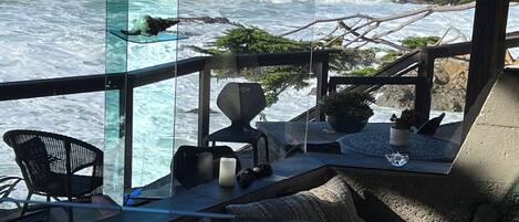 Vista al mar desde un balcón con paredes de cristal, que incluye un sofá, sillas y una mesa.