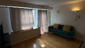 A room with a wooden floor, a green sofa with cushions, a radiator, and a window with curtains. - Beautiful 2 Bedroom - Woolwich (London)