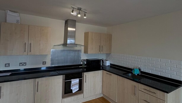 A kitchen with wooden cabinets, a black countertop, and a stainless steel range hood. - Beautiful 2 Bedroom - Woolwich (London)
