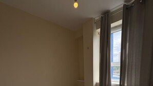 A single bed with a headboard, a bedside table, a window with curtains, and a light fixture. - Beautiful 2 Bedroom - Woolwich (London)