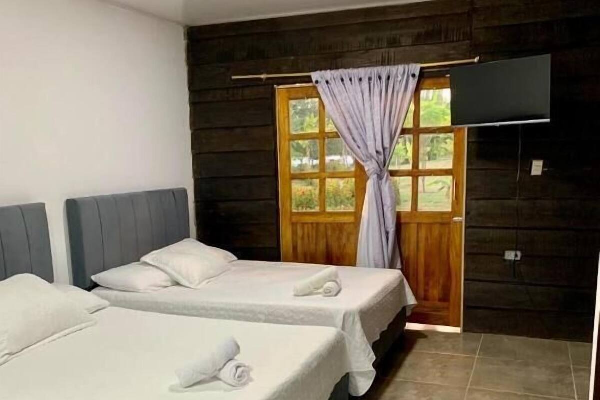 Una habitación de hotel con tres camas, una puerta de madera y suelo de baldosas.