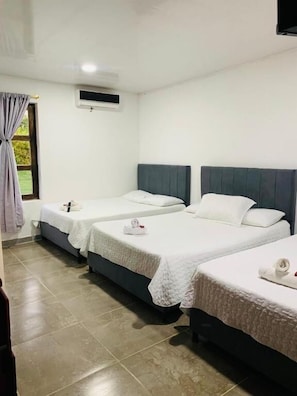 A hotel room with three single beds, a window with curtains, an air conditioning unit, and a tiled floor.