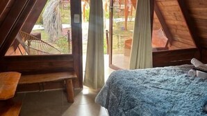 A bedroom with a bed, a wooden bench, a window with curtains, and a view of the outside. - Hotel Luna Azul Tatacoa  (Villavieja)