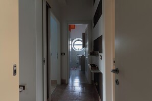 Ein Flur mit einer Tür links, einem Fenster mit Rundblick und einem Regal mit Gegenständen rechts.