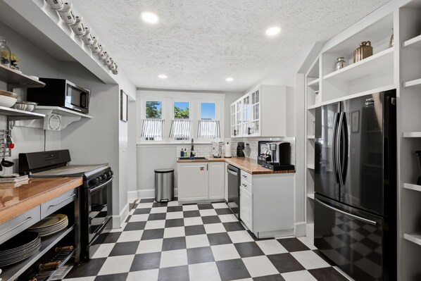 Una cocina moderna con piso a cuadros blanco y negro, electrodomésticos de acero inoxidable y alacenas blancas.