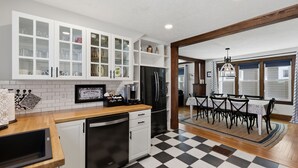 A kitchen with white cabinets, a black refrigerator, a wooden countertop, and a dining area with a table and chairs.