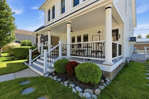 A two-story house with a covered porch, a front yard with a stone pathway, and a small garden with shrubs. - Dragonfly Guest House - Heart of GOTL (Geneva)