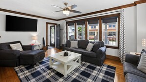 A modern living room with dark sofas, a white coffee table, and large windows with a view of buildings.