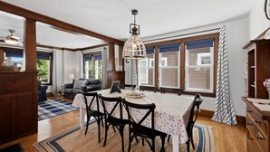 A dining area with a table set for four, wooden beams, large windows, and a ceiling fan.