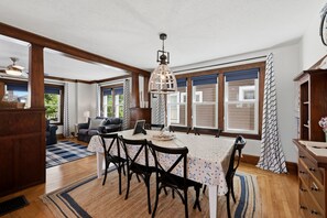 A dining area with a table set for four, wooden beams, large windows, and a ceiling fan. - Dragonfly Guest House - Heart of GOTL (Geneva)