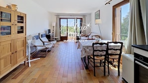 A room with a dining table, chairs, a kitchen area, a wooden cabinet, and a sliding glass door leading to an outdoor area. - Mazet T2 for 4 people with balcony in Cavalière (Le Lavandou)