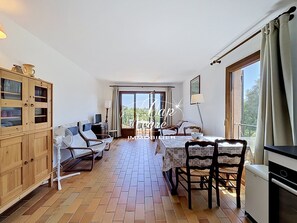 A room with a dining table, chairs, a kitchen area, a wooden cabinet, and a sliding glass door leading to an outdoor area. - Mazet T2 for 4 people with balcony in Cavalière (Le Lavandou)