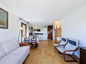 A living room with a sofa, chairs, a dining table, and a kitchen in the background. - Mazet T2 for 4 people with balcony in Cavalière (Le Lavandou)