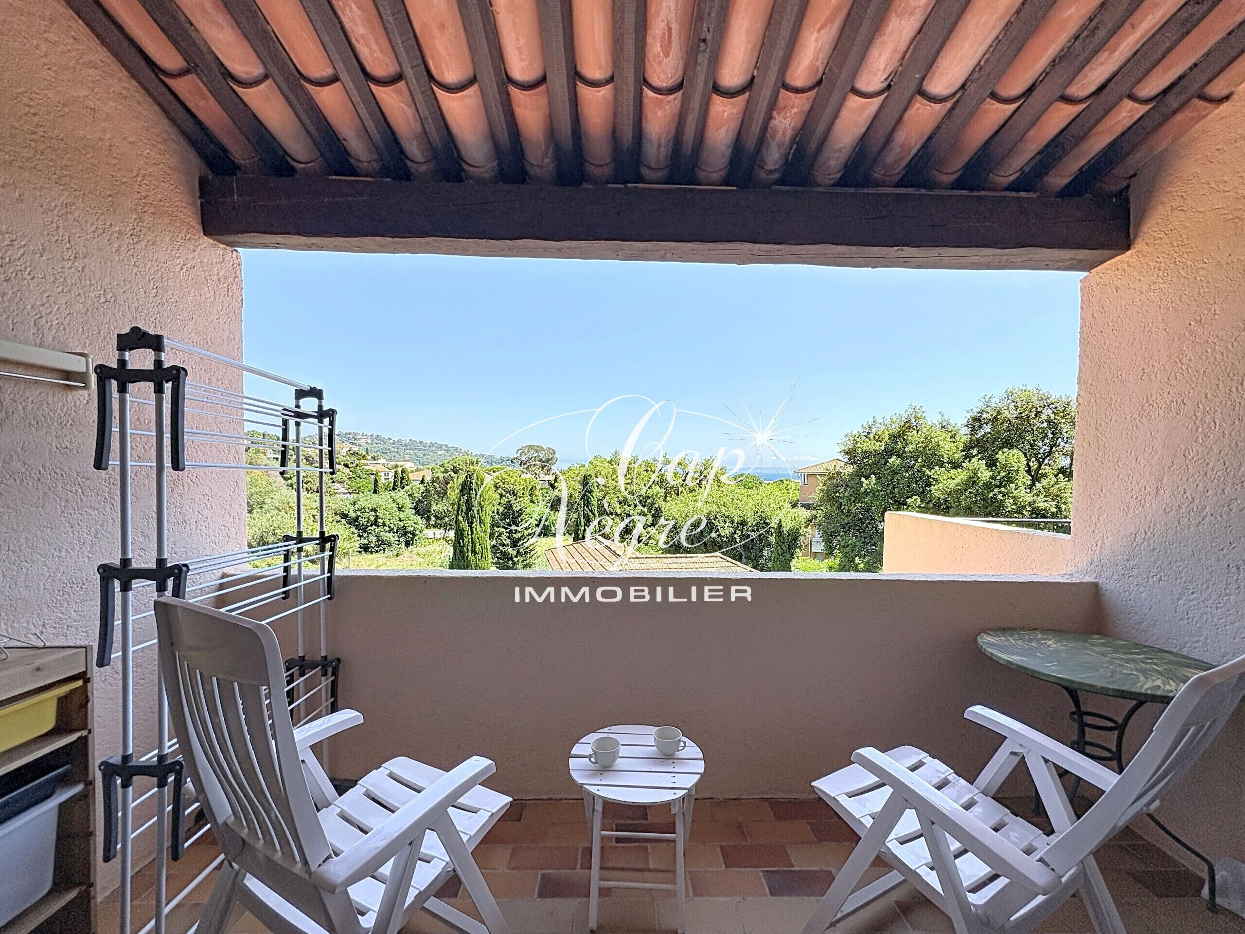 Un balcon donnant sur un vignoble, avec des chaises blanches, une petite table et un étendoir.
