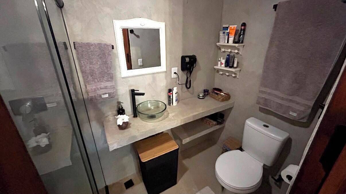 Un baño con un lavabo de vidrio, un inodoro, un espejo y un perchero para toallas.