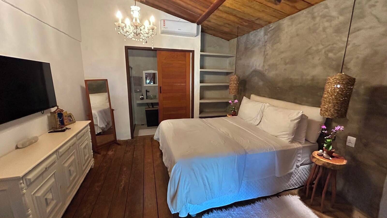 A bedroom with a bed, dresser, TV, chandelier, and a closet.