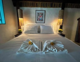 A neatly made bed with towels and a flower, framed artwork on the wall, and two wall-mounted lamps.