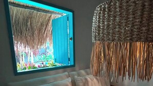 Ein Zimmer mit einem Holzsofa, einer gewebten Pendelleuchte und einem Fenster mit Gartenblick.