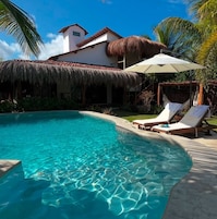 A clear swimming pool with lounge chairs and a thatched-roof structure.