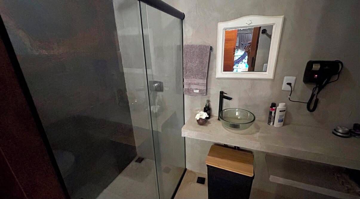 Casa de banho com cabine de duche em vidro, lavatório com espelho em cima e telefone fixo na parede.