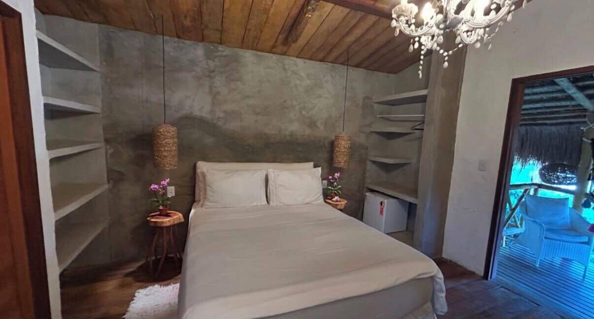 A bedroom with a bed, two bedside tables, a chandelier, and a view of a balcony.
