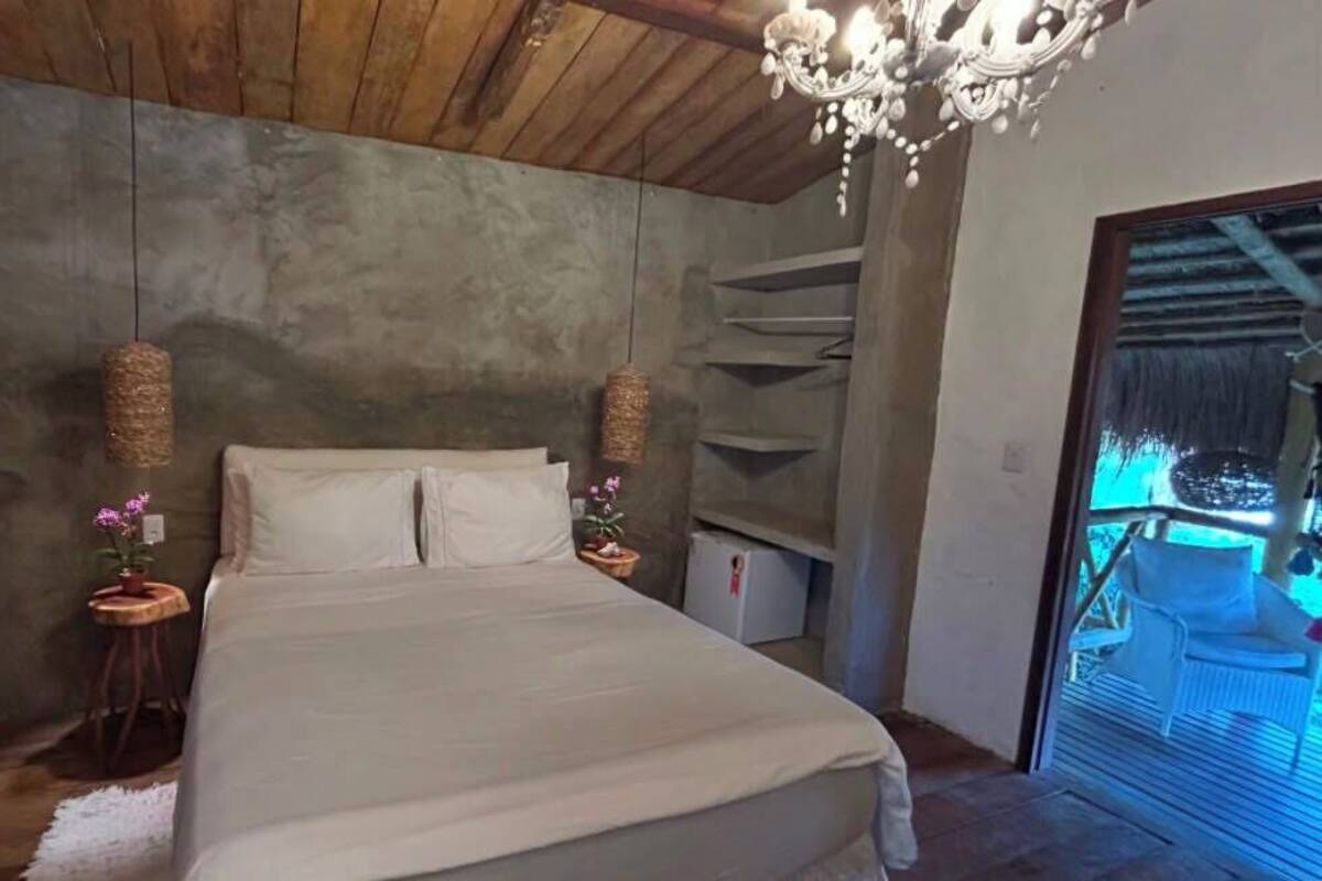 A bedroom with a bed, two bedside tables, a chandelier, and a view of a balcony.