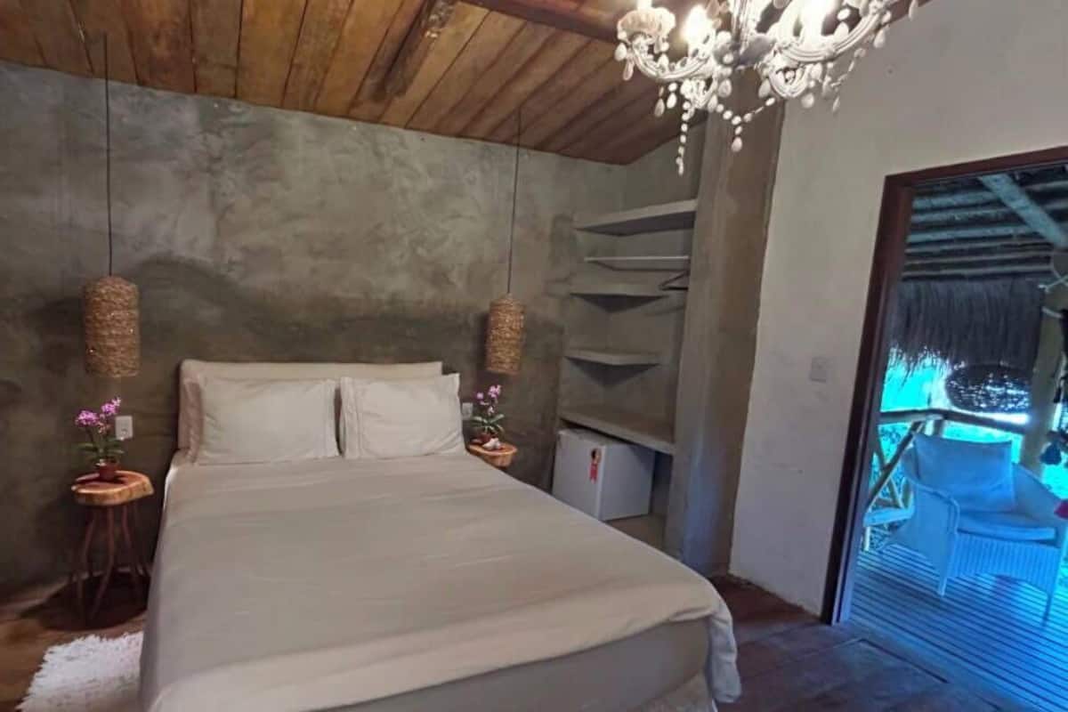 A bedroom with a bed, two bedside tables, a chandelier, and a view of a balcony.