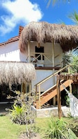 A thatched-roof building with a wooden staircase leading to a balcony.