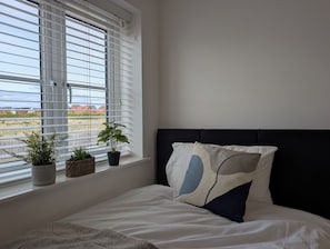 Une chambre avec un lit, une fenêtre avec des stores et deux plantes en pot sur le rebord de la fenêtre.