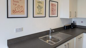 Cozinha com pia, quadros nas paredes e armários brancos.