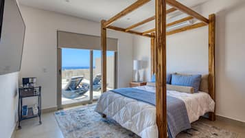 A bedroom with a four-poster bed, a large window, and a view of the sea.