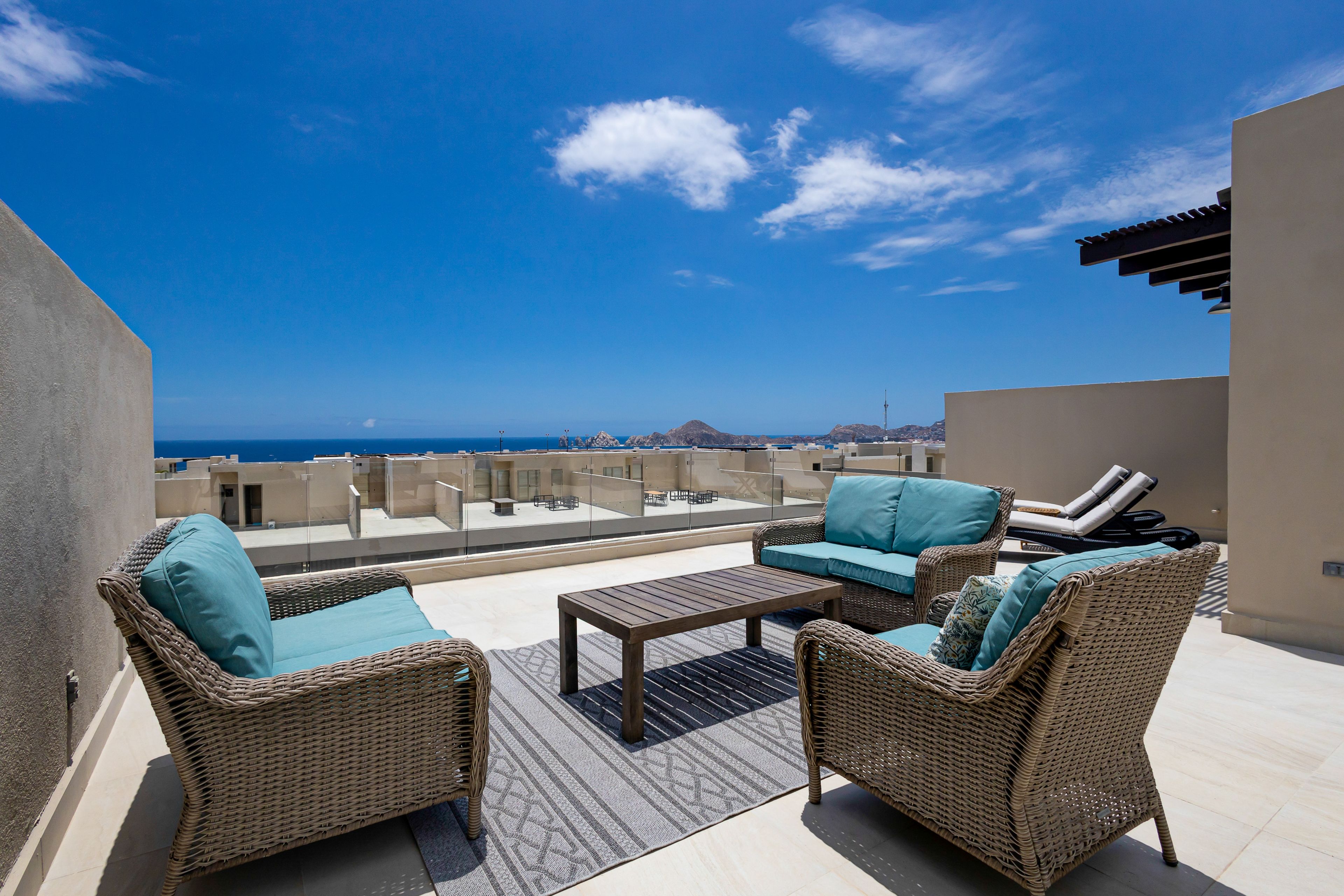 A rooftop terrace with wicker furniture, a coffee table, and a view of the ocean.