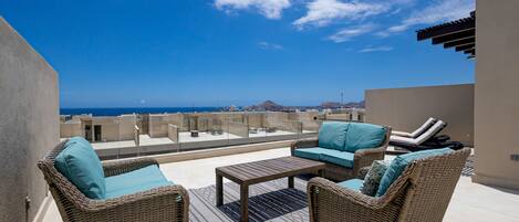A rooftop terrace with wicker furniture, a coffee table, and a view of the ocean.