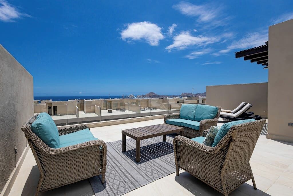 Eine Dachterrasse mit Korbmöbeln, einem Couchtisch und Blick aufs Meer.