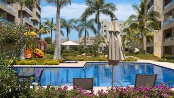 A swimming pool with lounge chairs, palm trees, and a playground.