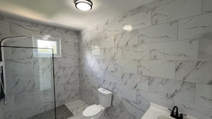 Ein Badezimmer mit Marmorfliesen, einer Duschkabine aus Glas, einer Toilette und einem Waschbecken.