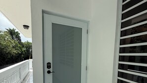 Eine weiße Tür mit einer geätzten Glasscheibe, einem Zahlenschloss und einem kleinen Fenster mit horizontalen Rollläden.