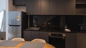 Une cuisine moderne avec des meubles de couleur sombre, un réfrigérateur en acier inoxydable, un four encastré et un coin repas comprenant une table et des chaises.