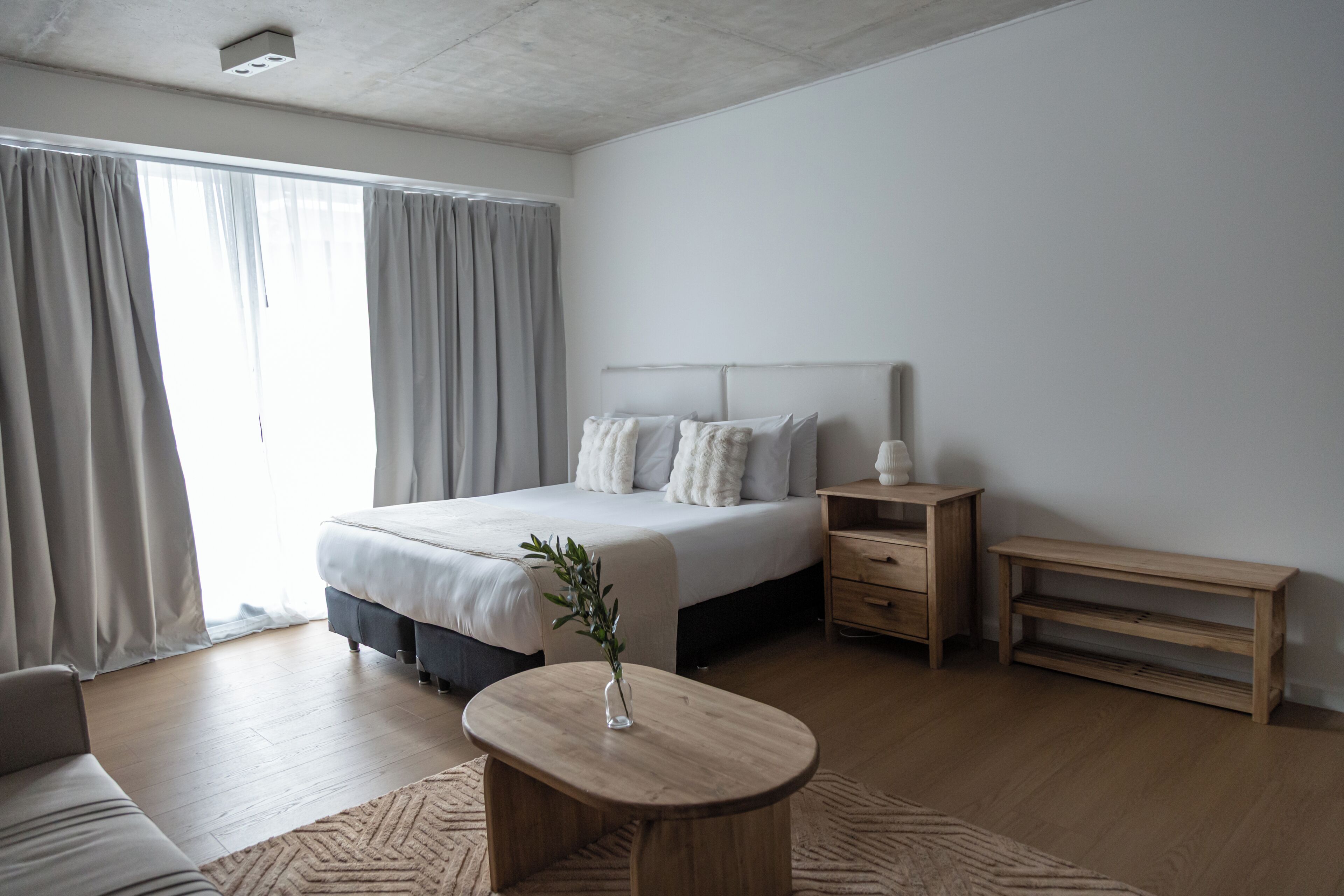 A modern bedroom with a bed, bedside tables, a wooden nightstand, and a round table with a vase.