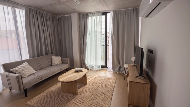 Un salon moderne avec un canapé, une table basse, un meuble pour la télévision et une grande fenêtre avec des rideaux.