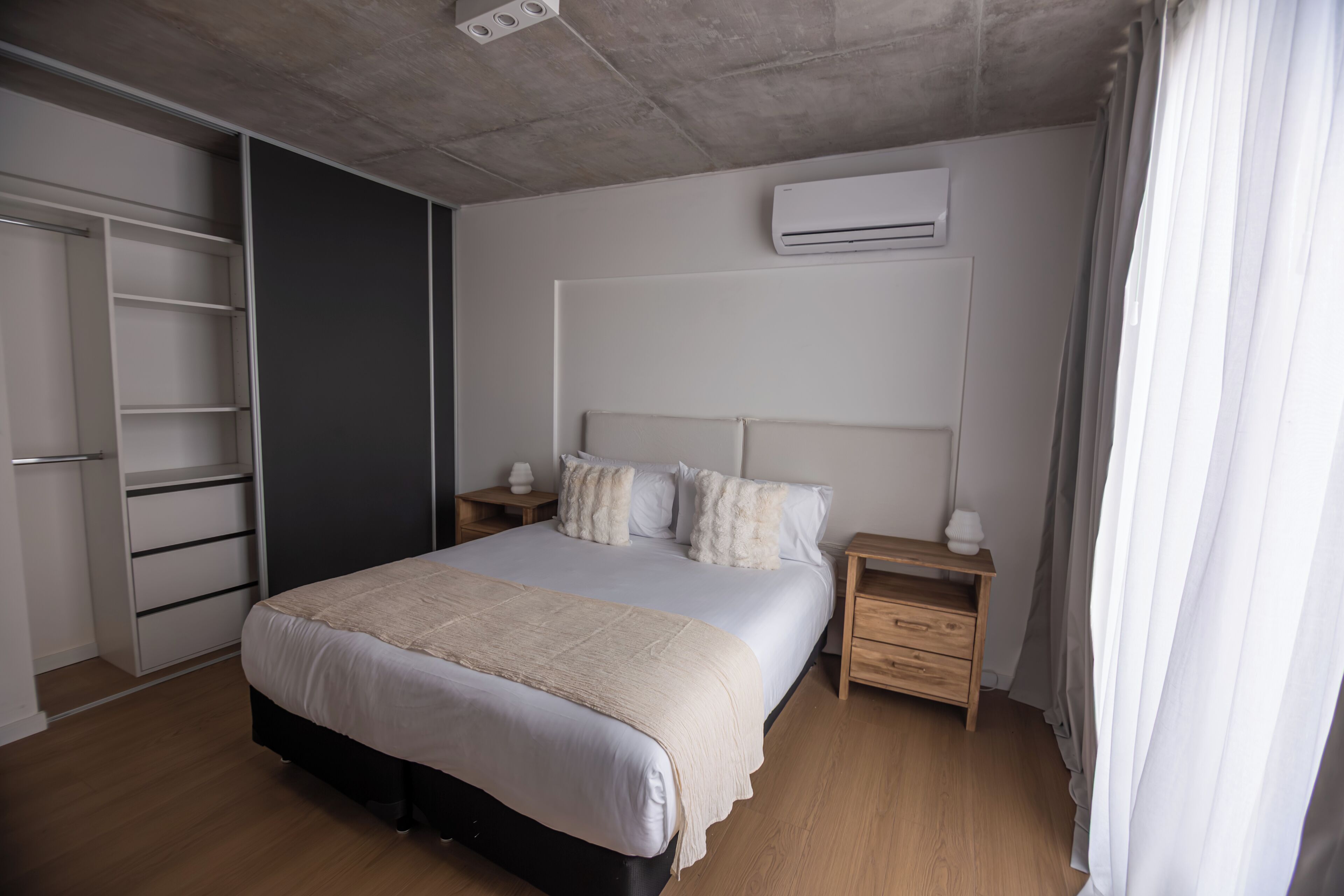 Un dormitorio con cama, mesitas de noche, armario y aire acondicionado.