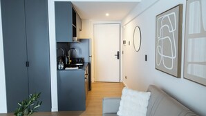 Une cuisine moderne avec des meubles gris, une porte blanche et un coin repas comprenant un canapé gris et un coussin blanc.