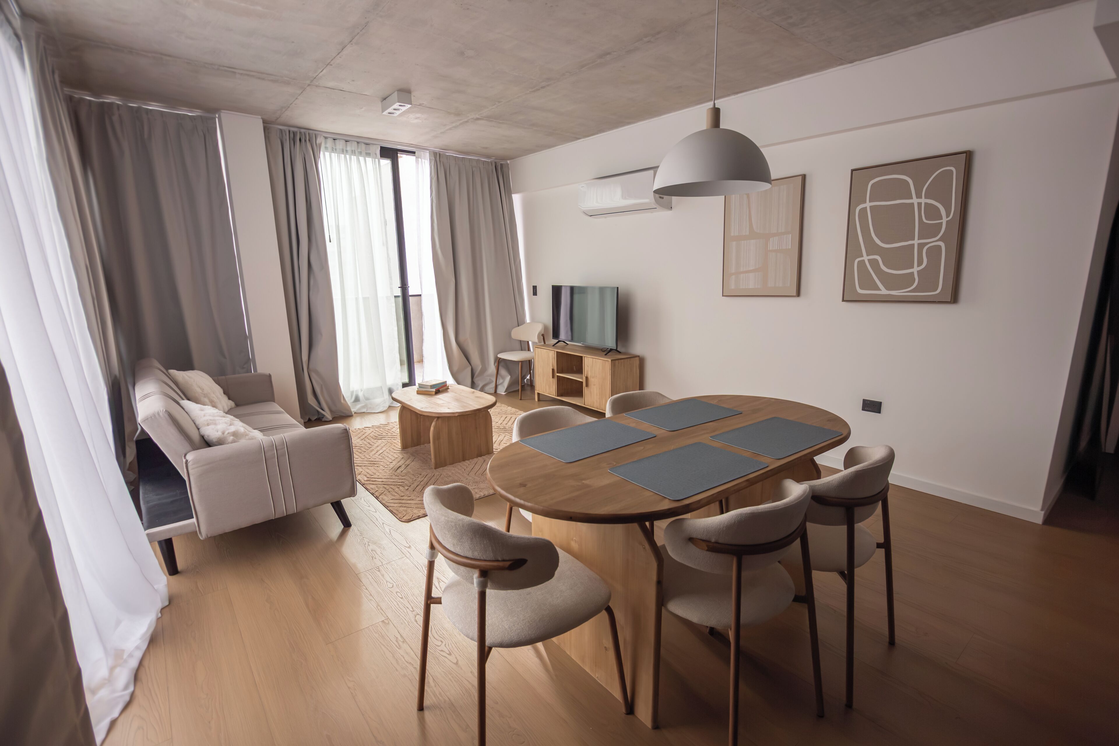 Una sala moderna con un sofá, una mesa de comedor con sillas, un televisor y obras de arte en la pared.
