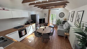 Une cuisine moderne avec des meubles blancs, une table à manger avec des chaises, un canapé, un téléviseur et une horloge au mur.