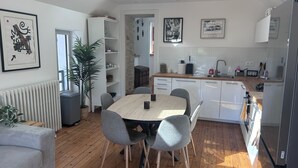 Une cuisine moderne avec des meubles blancs, une table à manger en bois, des chaises grises et une plante en pot.