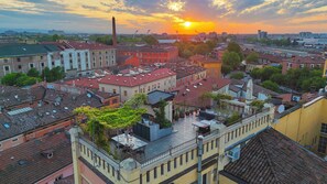 A cityscape with a prominent building featuring a rooftop terrace with outdoor seating. - Terrazza Bonasi | Relaxation & Cinema in the Historic Center (Modena)