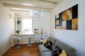 A modern living room with a grey sofa, two bar stools, a white spiral staircase, and a large abstract painting on the wall. - Terrazza Bonasi | Relaxation & Cinema in the Historic Center (Modena)