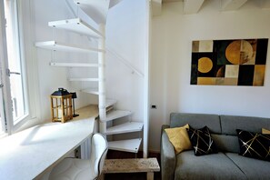 A modern interior with a staircase, a grey sofa with patterned cushions, and a wall art piece. - Terrazza Bonasi | Relaxation & Cinema in the Historic Center (Modena)